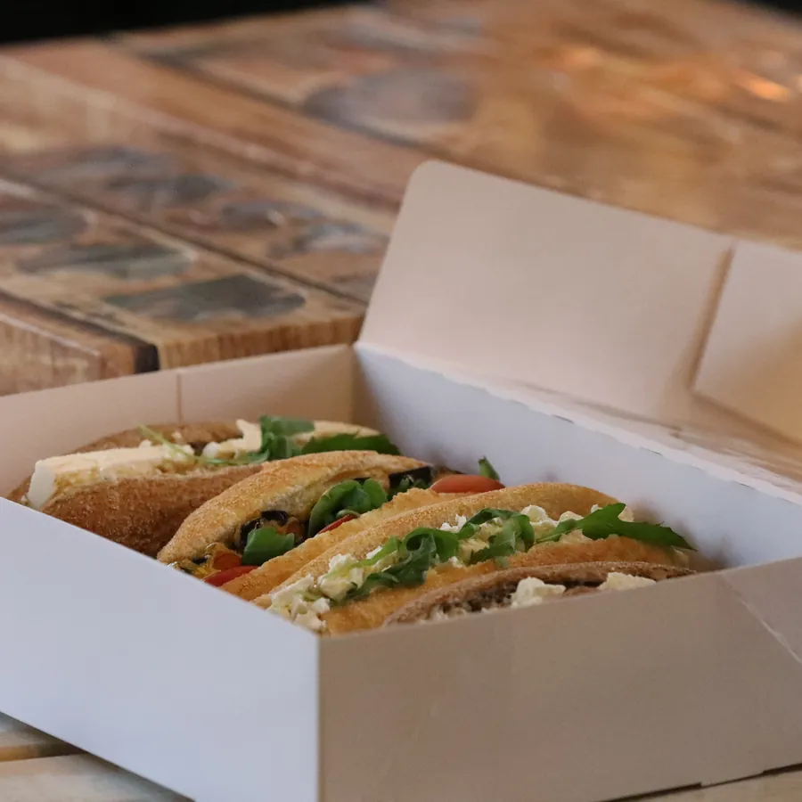 A catering box filled with wrapped sandwiches