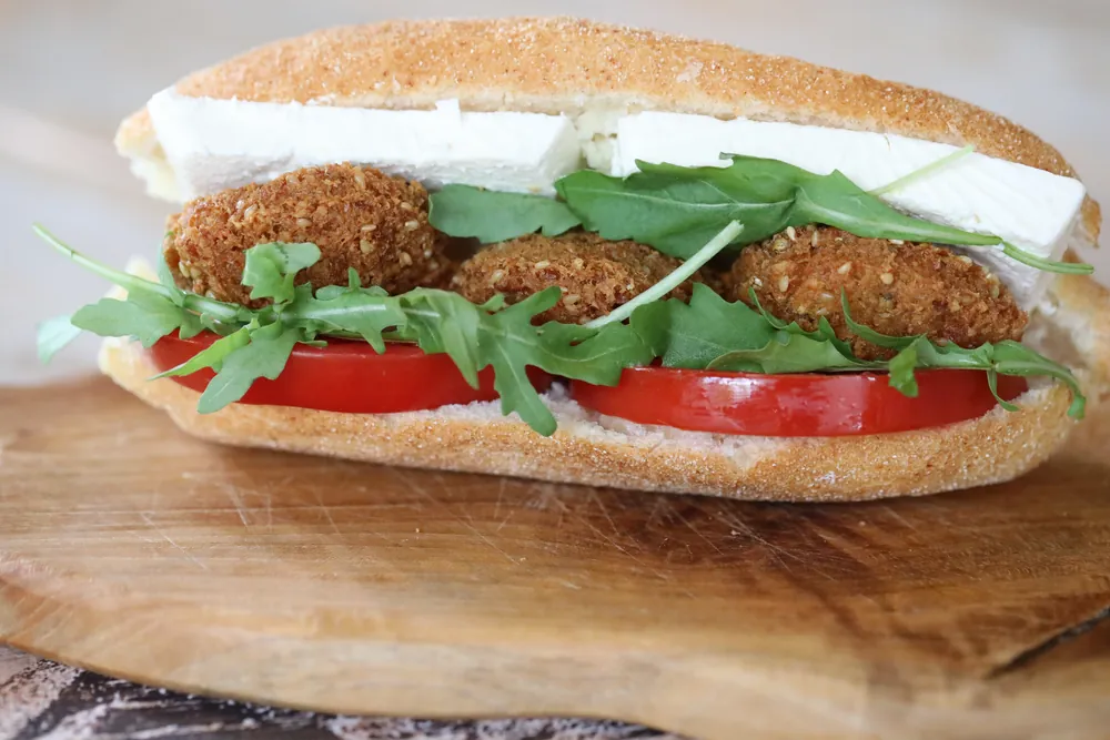 A falafel roll with rocket and tomato on a wooden board