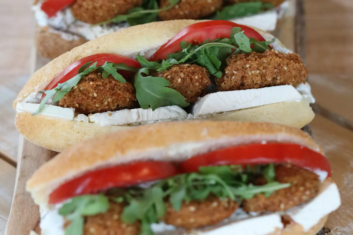 Three falafel sandwiches lined up on a board