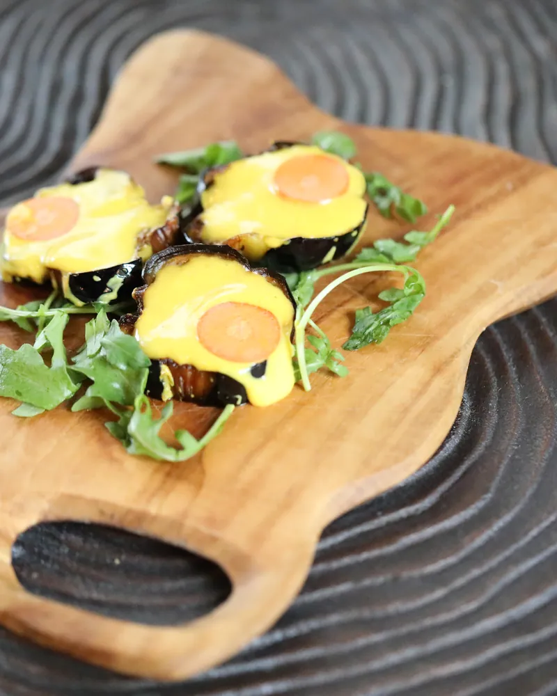 Glazed aubergine and egg on a carved serving board with rocket