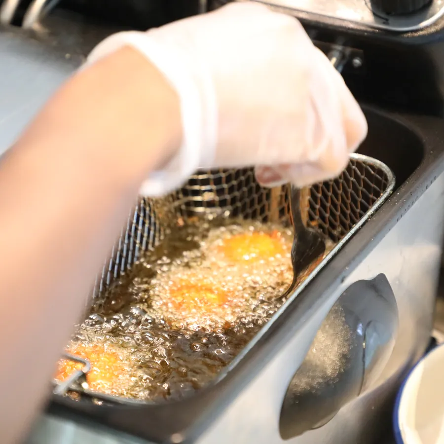 A cook lowering falafel into the fryer