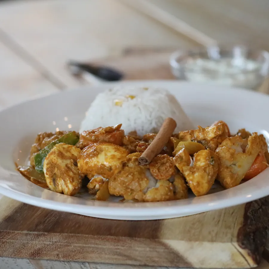 A plate of spiced chicken with rice and a side of yoghurt sauce