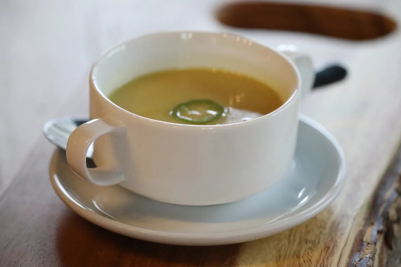 A cup of golden lentil soup with a slice of green chilli