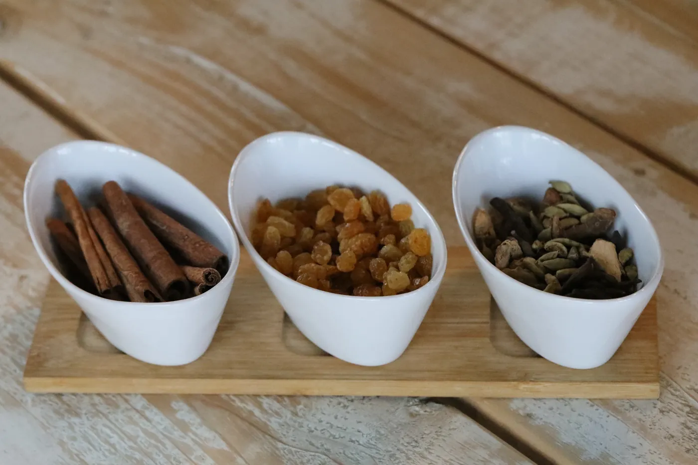 Bowls of spices and dried fruit beside cinnamon sticks